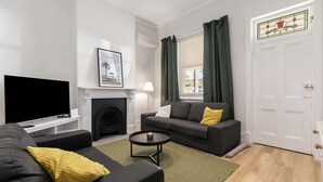 Un salon comprenant un canapé, un téléviseur, une cheminée, une fenêtre avec des rideaux et une porte ornée de vitraux.