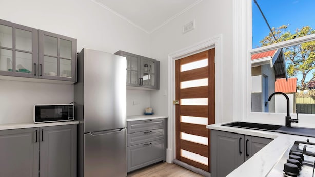 Une cuisine moderne avec des meubles gris, un réfrigérateur en acier inoxydable, un four à micro-ondes, un évier et une fenêtre donnant sur une maison.