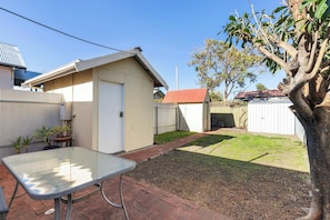 A backyard with a metal table, a shed, and a tree. - Cosy Glenelg South Family Cottage| Close To Beach | Pets Welcome (Glenelg South)
