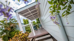 Une véranda couverte avec des marches menant à un espace patio, entouré de verdure et sous un ciel dégagé.