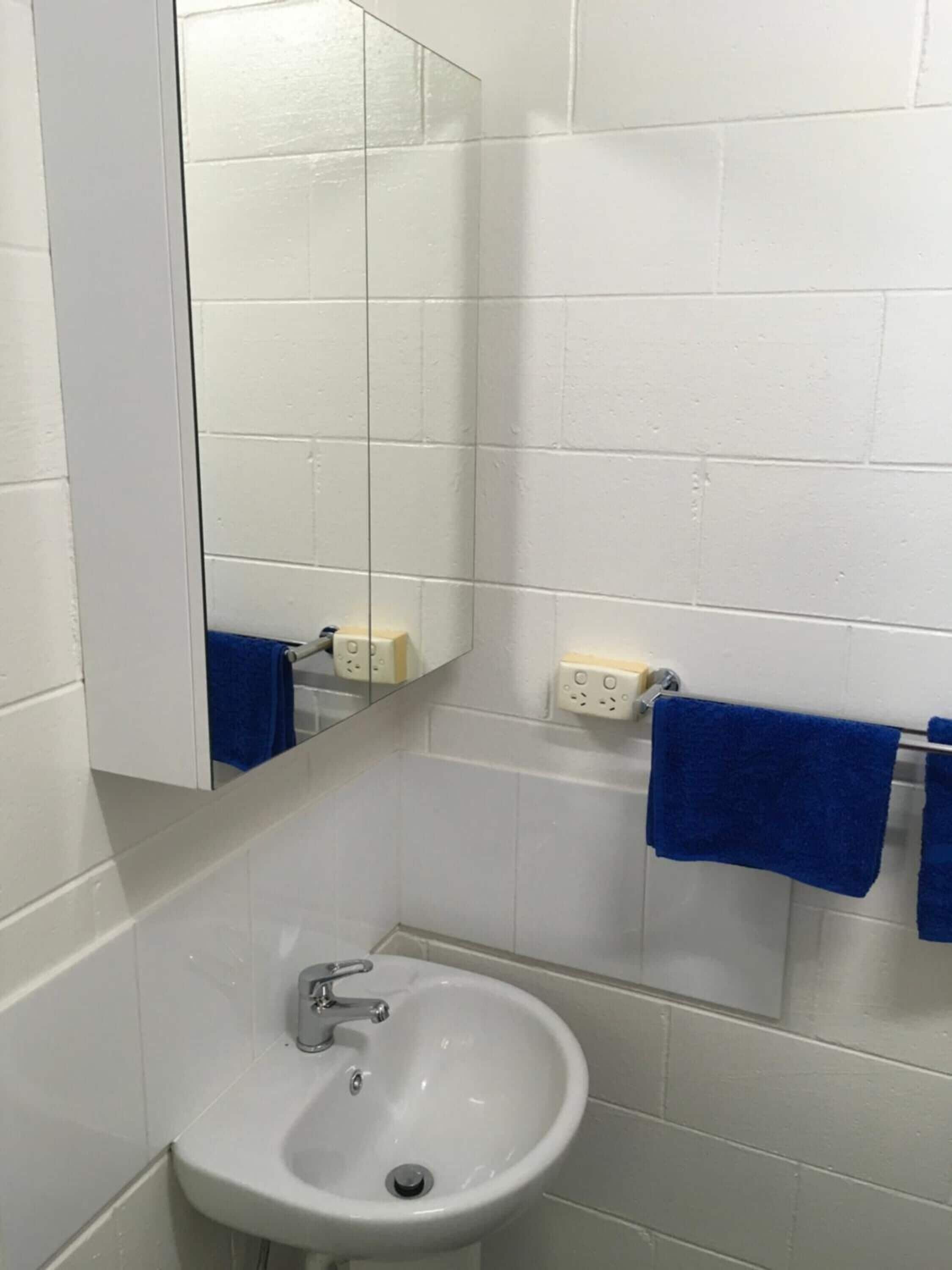 A bathroom with a white sink, a mirror, and two blue towels hanging on a rack.