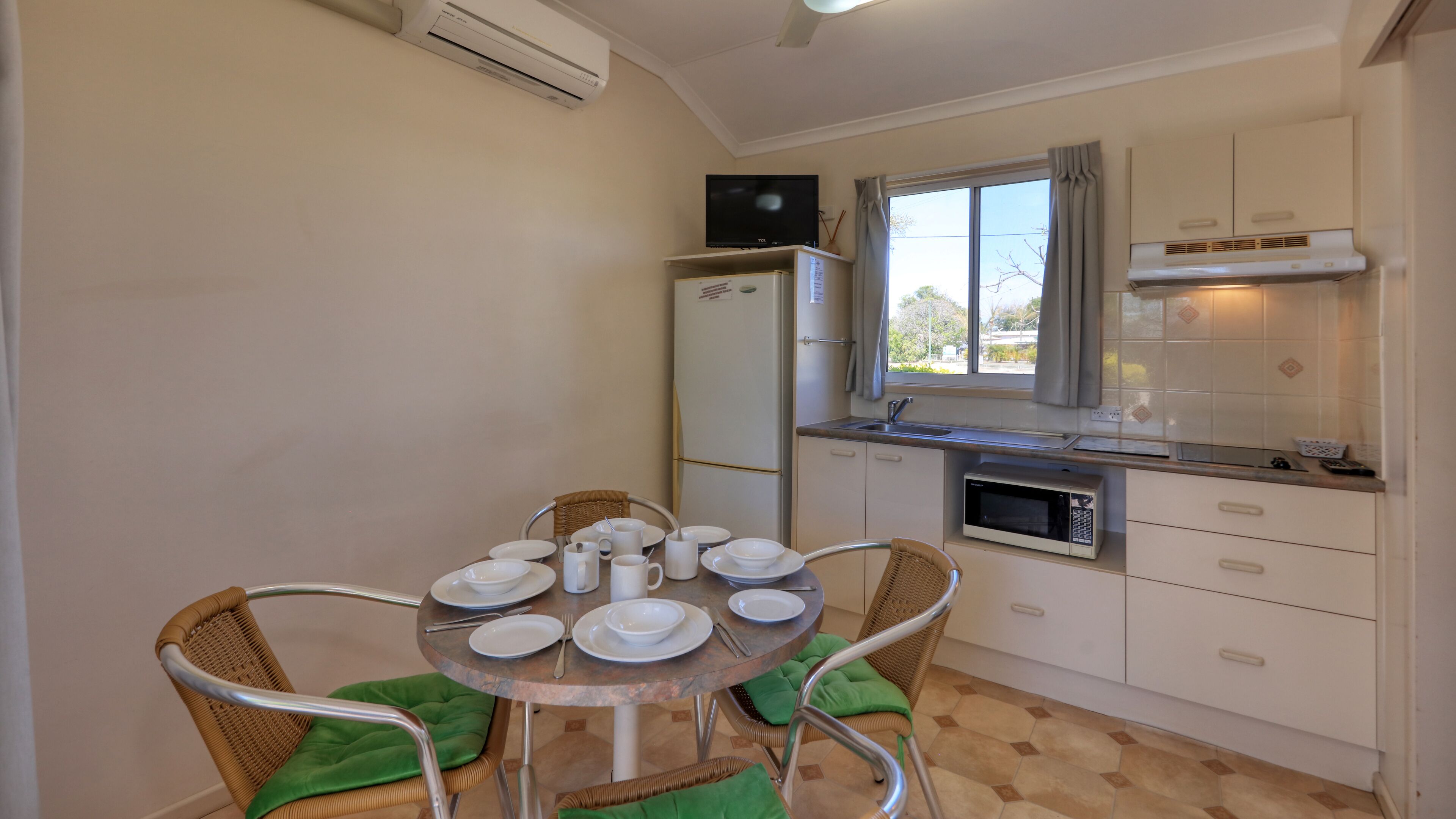 A compact kitchen with a dining area, a refrigerator, a microwave, and a window with curtains.