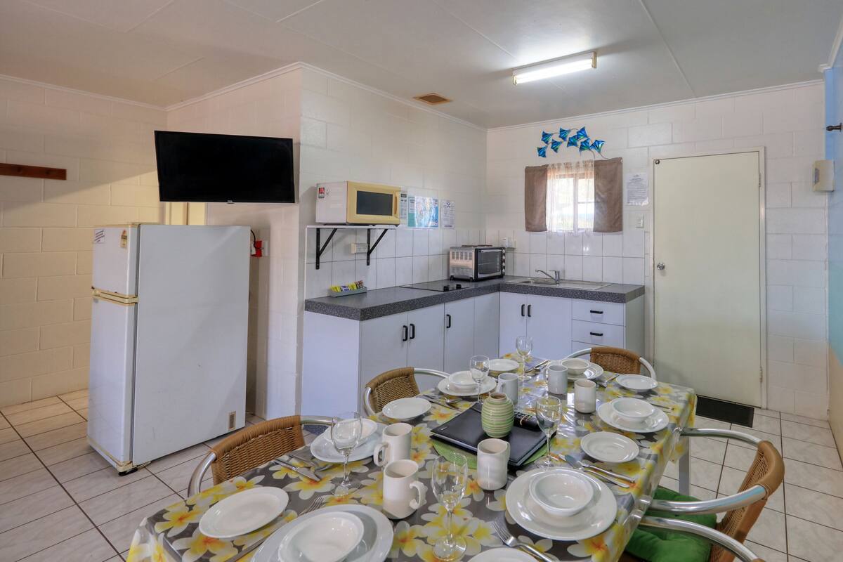 Una cocina compacta equipada con refrigerador, microondas y tostadora, y un comedor con una mesa dispuesta para cuatro personas.