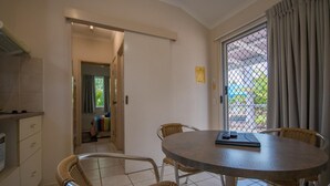 Un coin repas avec une table ronde et des chaises en osier, un coin cuisine équipé d’un four à micro-ondes, et une vue à travers une porte vitrée.