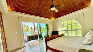 Ein Schlafzimmer mit Holzbalkendecke, einem großen Bett, einem Fernseher und Blick ins Freie.