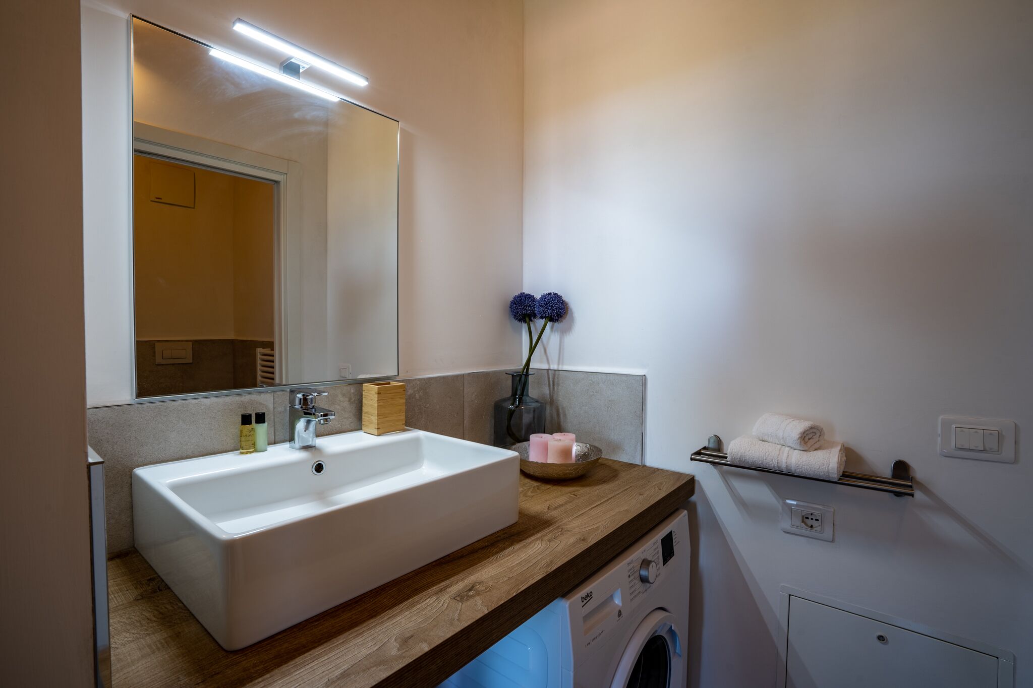 A modern bathroom with a large sink, mirror, and a washing machine.