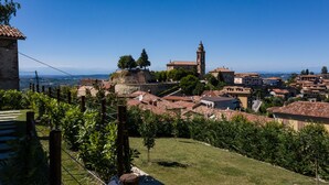 A historic town with terracotta-roofed buildings, a prominent tower, and a grassy hill with a fence in the foreground. - ONE BEDROOM HOLIDAY FLAT WITH VIEW (Diano d'Alba)