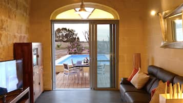 Un'ampia zona giorno con televisione, un divano e una porta vetrata scorrevole che si apre su un patio esterno con piscina.