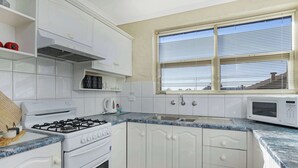 Een keuken met witte kasten, een fornuis, een magnetron en een raam met zonwering.