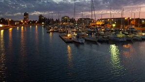 Een jachthaven in de schemering met aangemeerde boten, een stadsachtergrond en een rustig wateroppervlak dat lichtjes reflecteert.