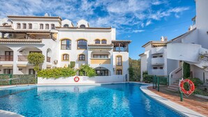 Une piscine entourée de bâtiments blancs dotés de balcons, un ciel bleu azur et une bouée de sauvetage placée au bord de la piscine.