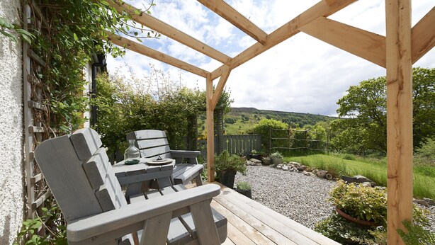Une terrasse en bois agrémentée d’une pergola, d’un espace salon extérieur et offrant une vue sur un paysage rural.