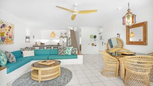 A modern living room with a sofa, coffee table, and wicker chairs. A ceiling fan and pendant light are visible.