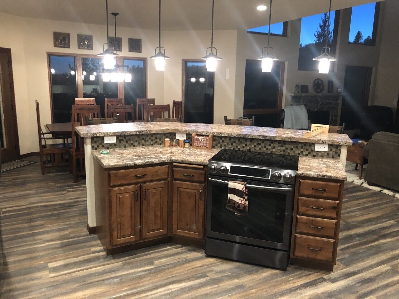 A kitchen with wooden cabinets, a built-in oven, granite countertops, pendant lighting, and a large window.