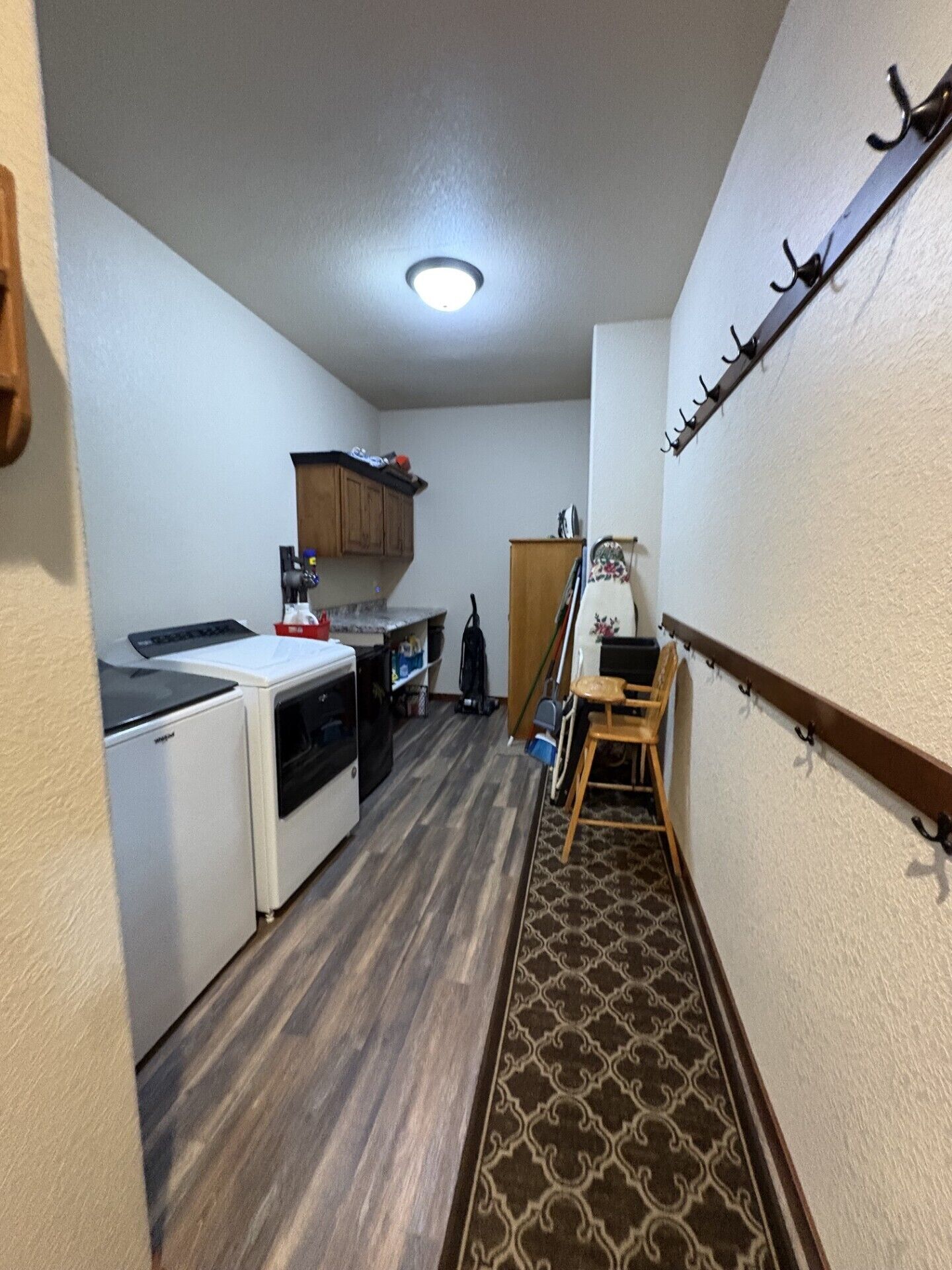 A narrow hallway with a microwave, a small refrigerator, a wooden chair, and a coat rack.