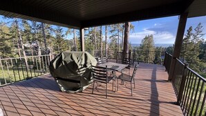 Eine überdachte Terrasse mit Grill, Gartenmöbeln und Blick auf Bäume und eine entfernte Landschaft.