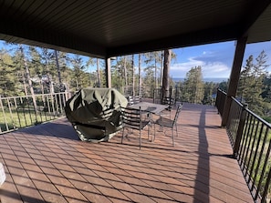 A covered deck with a grill, outdoor furniture, and a view of trees and a distant landscape.