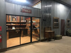 A rustic interior with a Coca-Cola sign, wooden shelves, and a large glass door leading to a kitchen area. - Cowboy corral at Rockin' star ranch (Brenham)