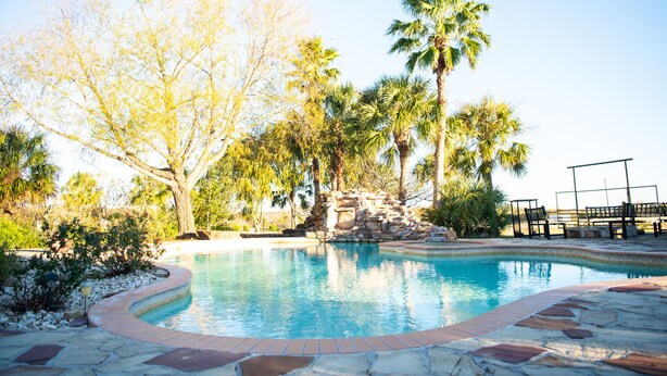 Piscina com borda de pedra, rodeada por árvores e uma formação rochosa.