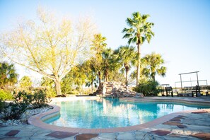 A swimming pool with a stone border, surrounded by trees and a rock formation. - Cowboy corral at Rockin' star ranch (Brenham)
