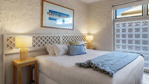 A bedroom with a bed, two bedside tables, a headboard, a window, and a framed picture on the wall. - Riverside Courtyard Glenelg North | Pets Welcome (Glenelg North)