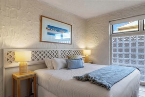 A bedroom with a bed, two bedside tables, a headboard, a window, and a framed picture on the wall.