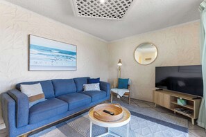 Una sala de estar con sofá, televisor, lámpara y un cuadro en la pared.