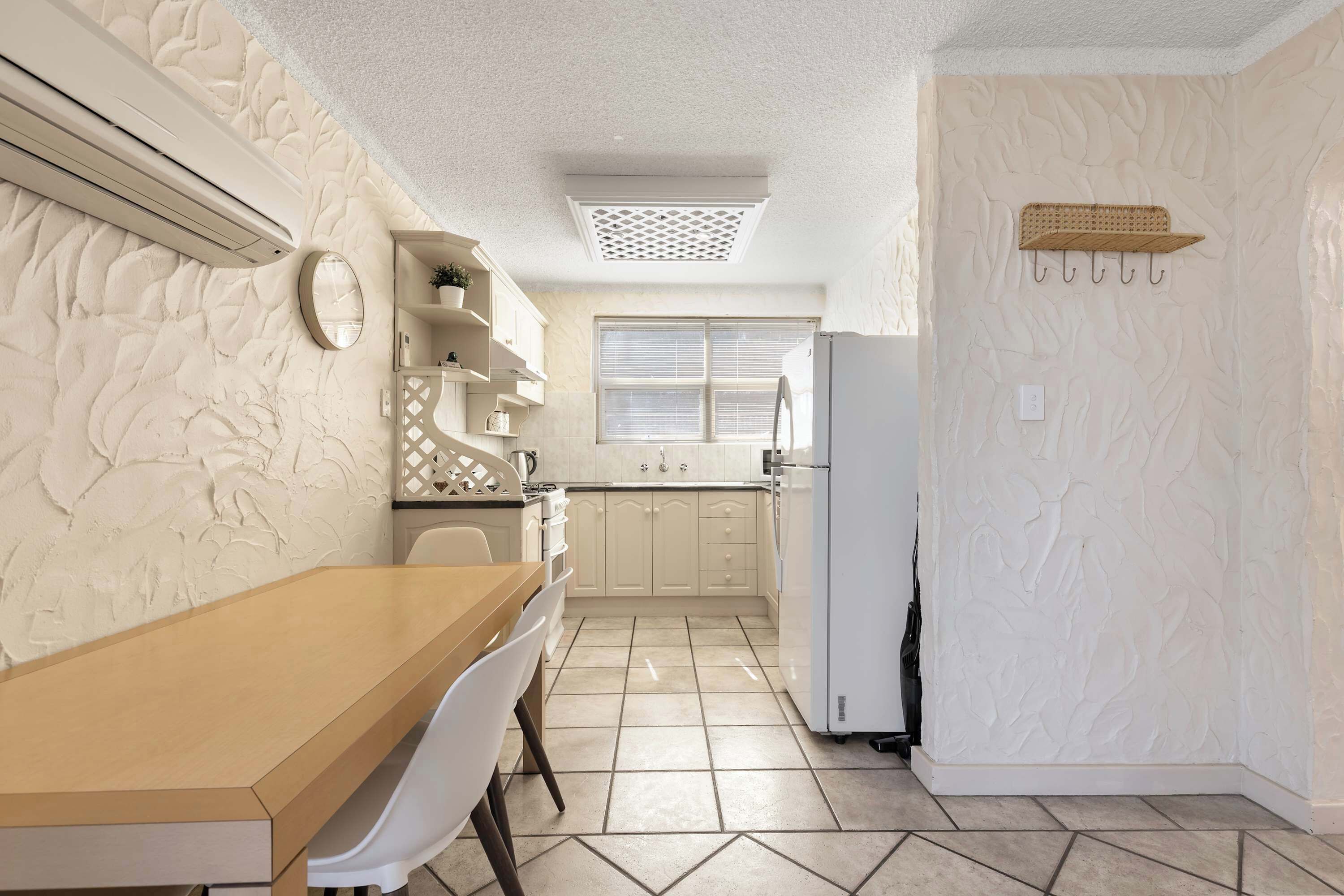 A kitchen with a wooden table, white chairs, a refrigerator, and a window with blinds.