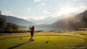 A golf course with a clear view of the surrounding mountains and a lake.