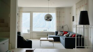 Una sala de estar moderna con un sofá, una mesa de centro y un ventanal con vistas a montañas.