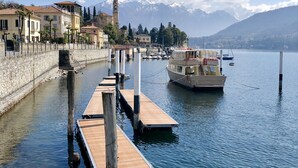 Un muelle frente al agua con barcos, un muro de piedra y edificios que incluyen una torre con reloj.
