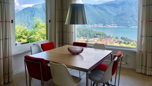 Un comedor con mesa y sillas, ventanas amplias con vistas a la montaña y una lámpara colgante.