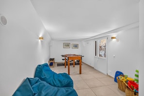 Une pièce avec une table de baby-foot, un canapé et une fenêtre donnant sur un mur en pierre.