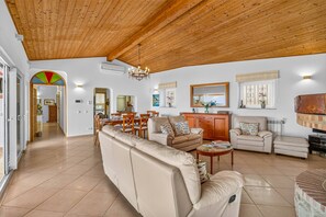A spacious living area with a high wooden ceiling, a dining area, and a kitchen in the background.