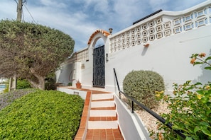 A white building with a black gate, a staircase leading to the entrance, and a well-maintained garden.