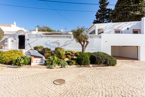 A white building with a tiled entrance, a small staircase, and a paved courtyard.