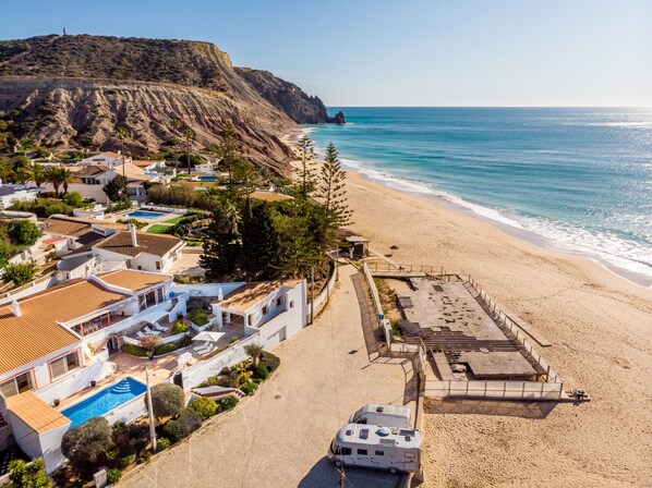 A coastal property with a swimming pool, beach access, and a view of the sea.