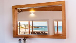 Een badkamer met een spiegel met houten lijst, die uitzicht op een strand weerkaatst.