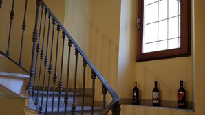 Un escalier orné de balustres travaillés, une fenêtre à croisillons et une étagère remplie de bouteilles.