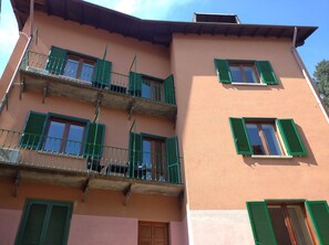 A multi-story building with balconies, green shutters, and a pink facade.