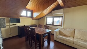 Une pièce avec un plafond en bois, une table à manger avec des chaises, un canapé, un téléviseur fixé au mur et une fenêtre avec un climatiseur.