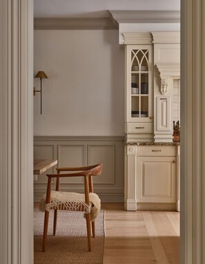 A kitchen with a wooden chair, a cabinet with glass doors, and a wall-mounted lamp.