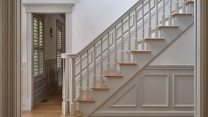 Una escalera con barandillas blancas y escalones de madera que conduce a un rellano con una puerta.