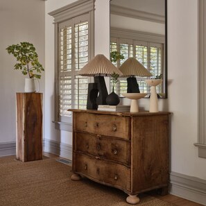 A wooden dresser with two lamps, a vase, and a book.
