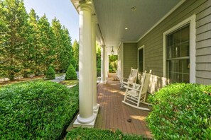 Een overdekt terras met witte zuilen, een houten terras en een rij witte schommelstoelen.
