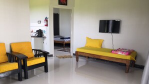 Ein Zimmer mit einem Bett, einem Sofa, einem an der Wand befestigten Fernseher und einer Küche im Hintergrund.