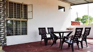 Eine überdachte Terrasse mit Tisch und Stühlen, ein Fenster mit Metallgitter und eine Ziegelwand.