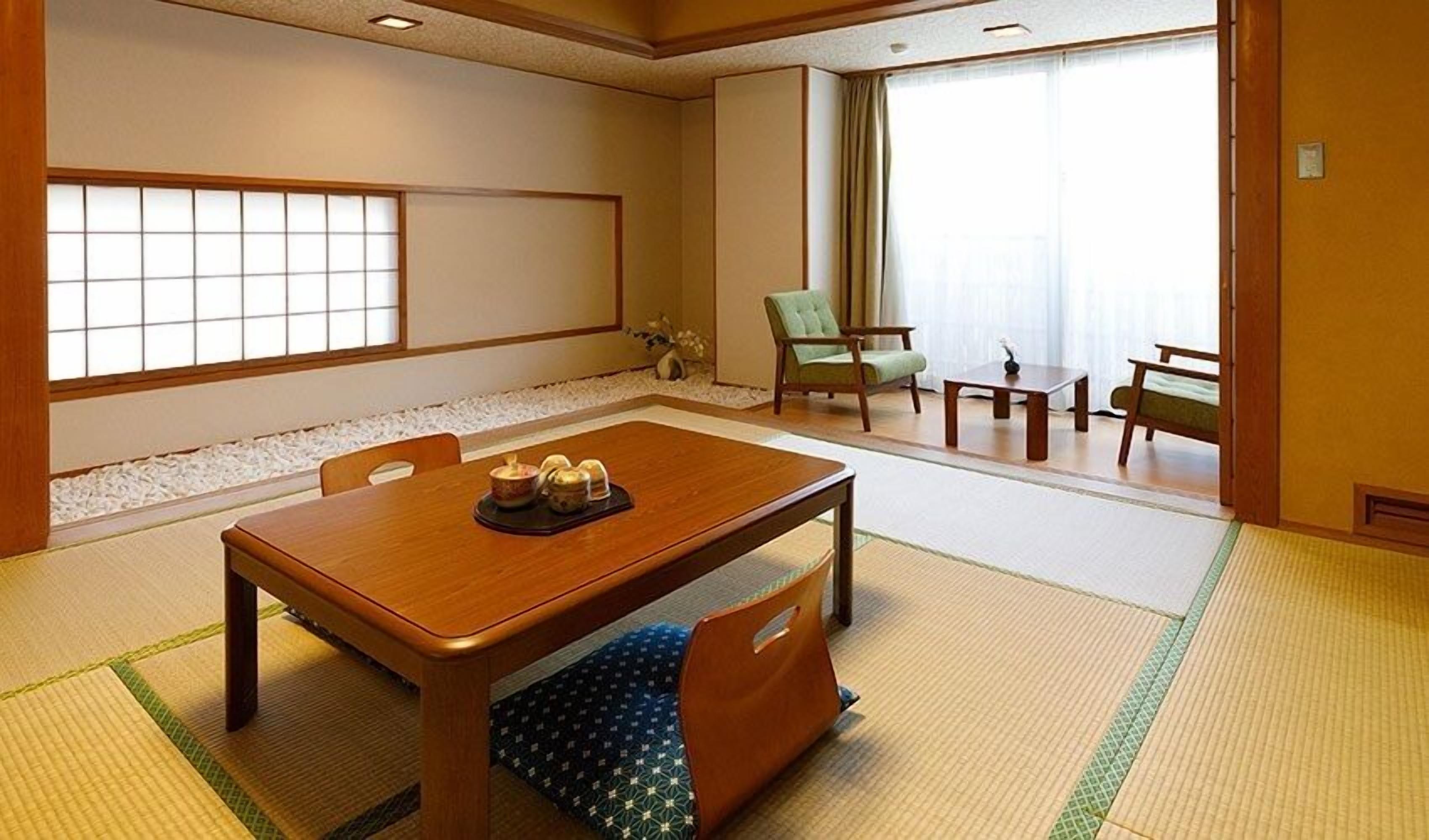 A traditional Japanese-style room with tatami flooring, a low table with cushions, a green chair, and a view of a garden through a shoji screen.