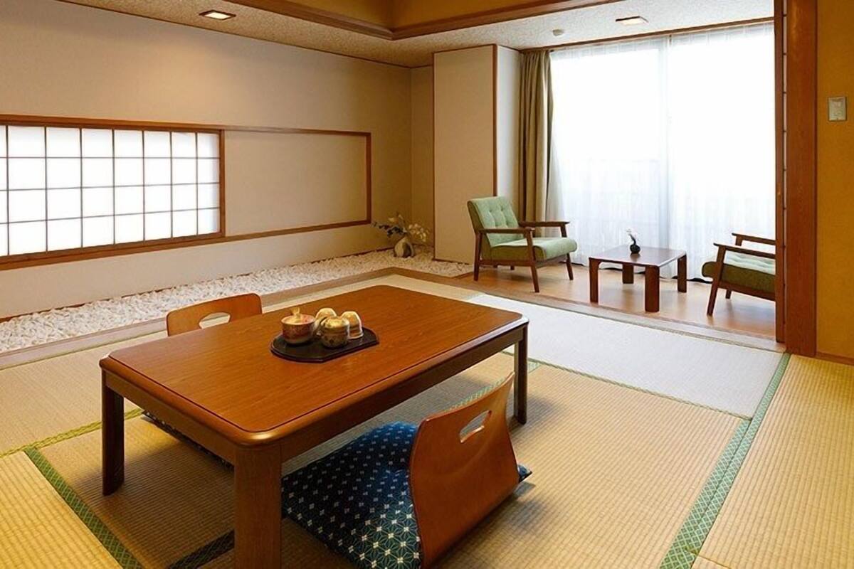 A traditional Japanese-style room with tatami flooring, a low table with cushions, a green chair, and a view of a garden through a shoji screen.