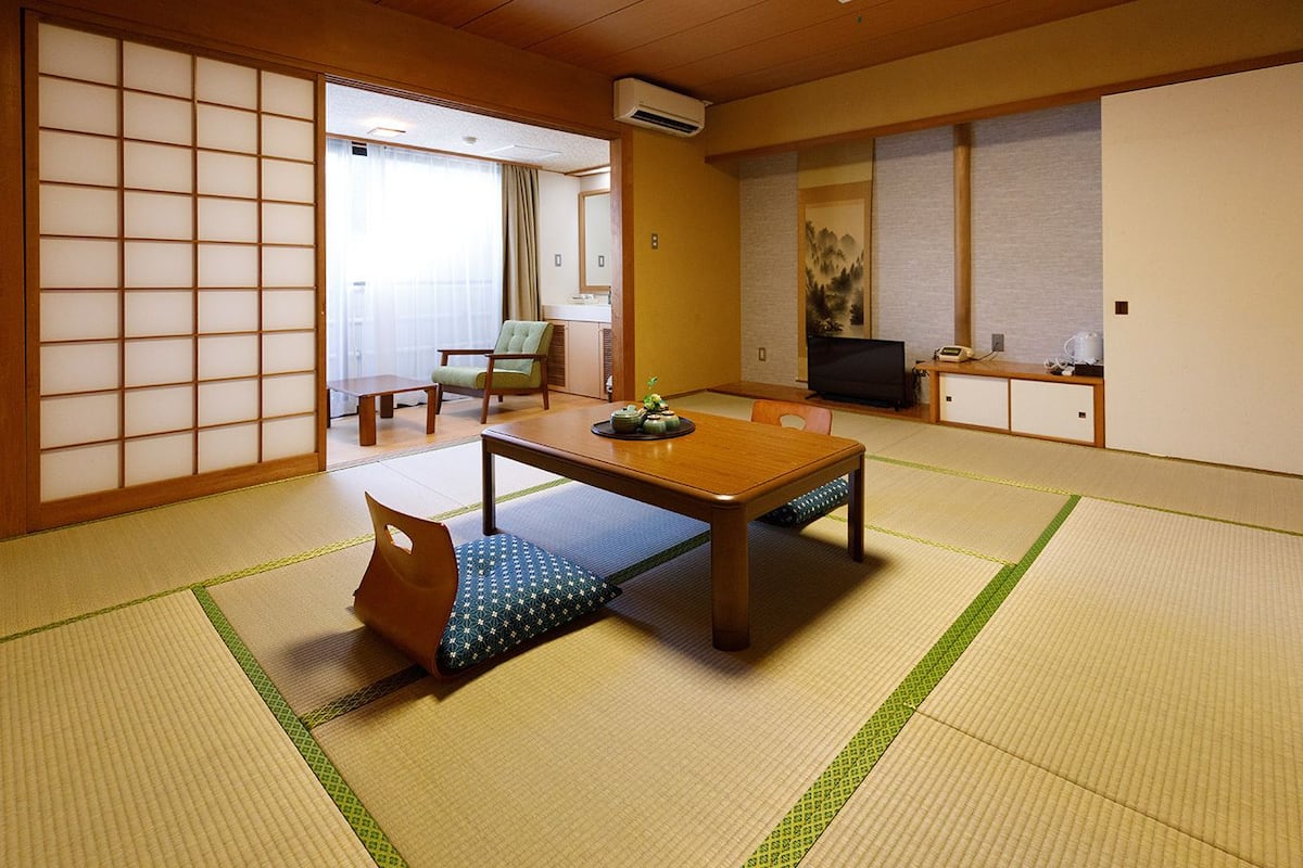 A traditional Japanese-style room with tatami flooring, a low table, a sofa, a television, and a sliding door.